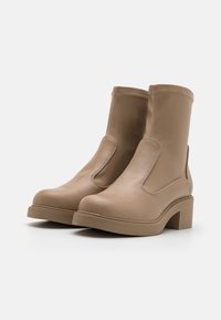 Bottines en cuir beige avec panneaux elastiques sur les côtés, bout arrondi et talon bloc épais. Texture lisse avec détails de couture contrastants.
