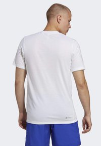 Witte korte mouwen t-shirt met een ronde hals, een gladde textuur en een licht getailleerd ontwerp, gezien vanuit de achterkant. In de onderste hoek staat een logo.