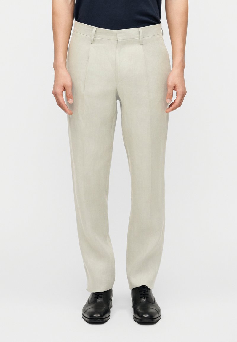 Pantalones de lino beige claro de corte recto, combinados con zapatos formales negros de cordones y una blusa negra metida, mostrados desde la cintura hasta los pies.