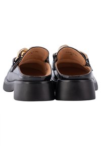 Paire de mocassins noirs en cuir verni avec talons épais et détail chaîne dorée, vus de dos sur fond blanc.