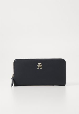 Tengerészkék bőrvállt, cipzáros záródással, arany színű logó díszítéssel az elején. Sima textúrájú és téglalap alakú.