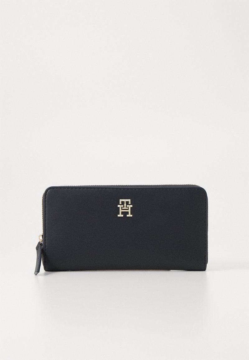 Navy leather wallet with zip closure, featuring a gold-tone logo accent on the front. Smooth texture and rectangular shape.
