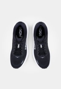 Chaussures de sport noires avec tige en maille, accents blancs, design à lacets et semelle rembourrée, arborant le logo "HOKA" sur le côté.