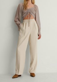 Ljusbrun, strukturerad blus med puffärmar och snörning fram; kombinerad med beige, högmidjade, vida byxor och bruna stövlar.