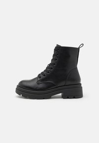 Svarte lær lace-up kampstøvler med kraftig såle og bøyle, sidevinkel på lys, ensfarget bakgrunn.