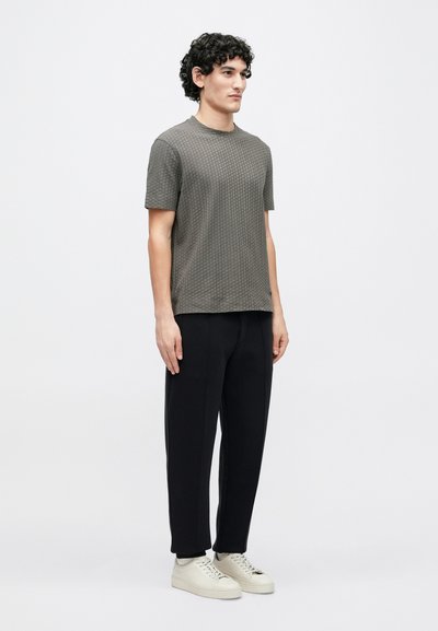 Γκρι υφασμάτινη κοντομάνικη μπλούζα με υφή, μαύρο παντελόνι και λευκά αθλητικά παπούτσια. Η μπλούζα διαθέτει γεωμετρικό μοτίβο και στρογγυλή λαιμόκοψη.