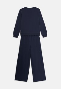 Mornarsko modra dolga majica s kratkimi rokavi v kombinaciji s spodnjimi hlačami širokega kroja, ležijo na beli podlagi.