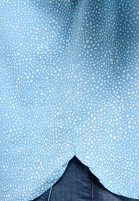 Helles blaues Hemd aus strukturiertem Stoff mit weißen gesprenkelten Mustern. Abgerundeter Saum mit leichtem Schlitz an den Seiten, kombiniert mit Denim.