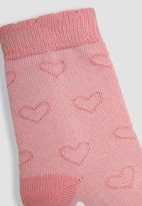 Calcetín de punto rosa con puño elástico, con patrones de corazones en relieve. Textura suave, color sólido y diseño sin costuras en la punta.