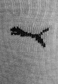 Primer plano de una tela de punto gris con un logotipo negro de Puma cosido en el material.