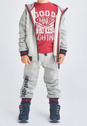 Grå bomulds-hoodie med røde og marineblå accenter, kombineret med grå joggingbukser med marineblåt print. Rød t-shirt med hvidt grafisk tryk. Marineblå sneakers.