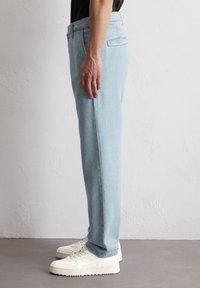 Jasnoniebieskie dżinsy o prostym kroju, z tylną kieszenią i subtelnymi detalami szycia, w połączeniu z białymi sneakersami.