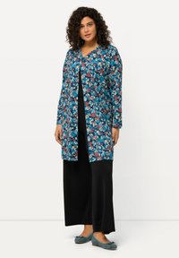 Cardigan largo floral con base azul y patrones rojos y blancos, combinado con pantalones anchos negros y zapatos planos azules. Textura de tela suave.