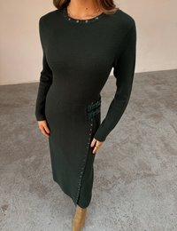 Σκούρο πράσινο πλεκτό φόρεμα με μακριά μανίκια, στρογγυλή λαιμόκοψη, διακοσμητικά κουμπιά στο πλάι και ιμάντες με αγκράφες στη μέση. Λείο ύφασμα.