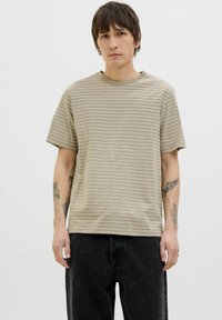 Beige striped t-shirt with a round neck, short sleeves, and a relaxed fit, worn over dark jeans. Fabric has a smooth texture.
