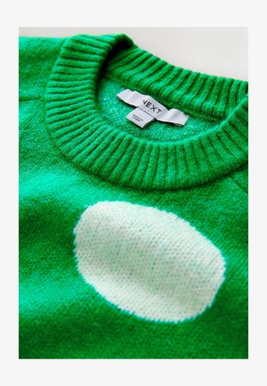 Grüner Strickpullover mit weißem ovalem Muster und einem umgeschlagenen Kragen, der ein weißes Kleidungsetikett zeigt.