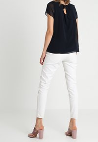 Top marinero de manga corta con diseño de abertura en la espalda, combinado con pantalones ajustados blancos y sandalias de tacón bloque rosa claro.