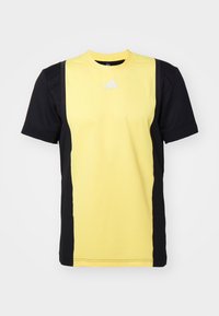 Camiseta deportiva de manga corta con un frontal amarillo, laterales negros, tejido texturizado y un logo blanco en el pecho.