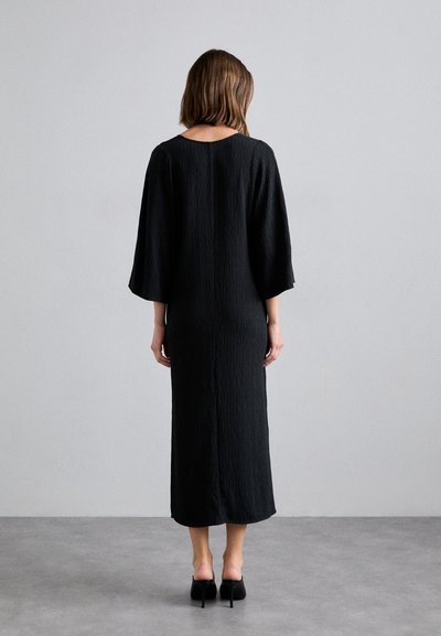Vestido maxi negro con tejido texturizado, mangas anchas y un escote redondo. Presenta una silueta simple y ajustada.