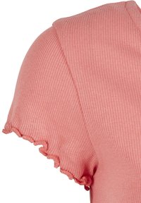 Gros plan d'un haut en tissu doux rose côtelé à manches courtes avec un ourlet à bordure ondulée.