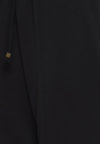 Zwarte joggingsbroek van zacht materiaal, met een elastische tailleband met koord en gouden metalen accenten.