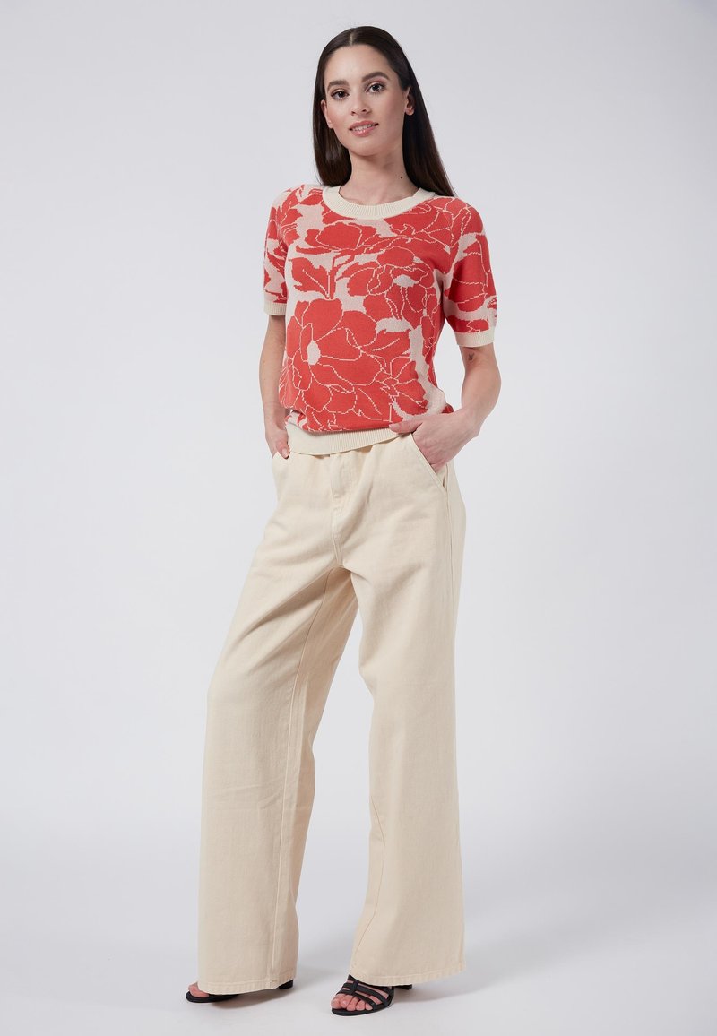 Red floral patterned knit top with short sleeves, paired with cream wide-leg pants. Black strappy sandals complete the look.