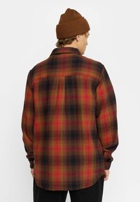 Rood, zwart en geel geruite flanellen shirt met een button-down kraag en lange mouwen. Zachte textuur, ronde zoom en details van de schouderpas.