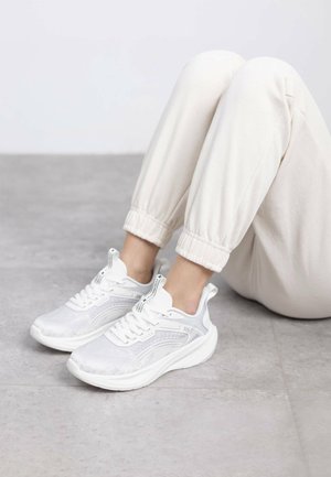 Zapatillas deportivas blancas con parte superior de malla, suela acolchada y acentos de diseño elegantes. Combinadas con pantalones de chándal color crema.