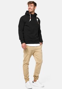 Zwarte hoodie met aantrekkoorden en een logo aan de voorkant, gecombineerd met lichtbeige joggers en witte sneakers. Soepele textuur, casual pasvorm.