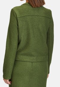 Green wool-blend jacket with a textured finish, featuring a collar, back seams, and a structured fit. The design has a minimalist style.