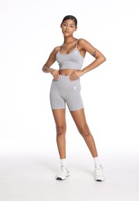 Grafitowy sportowy crop top i szorty high-waisted wykonane z elastycznego materiału. Posiadają subtelną grafikę na obu elementach. Ubrano z białymi sneakersami.