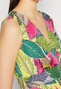Robe sans manches présentant un motif vibrant de feuilles tropicales multicolores sur un fond jaune, avec un décolleté en V profond.
