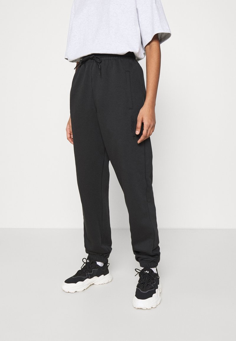 Svarta sweatpants med elastisk midja, dragsko och sidofickor; avsmalnande bendesign; mjuk tygtextur. Bärs med svarta sneakers.