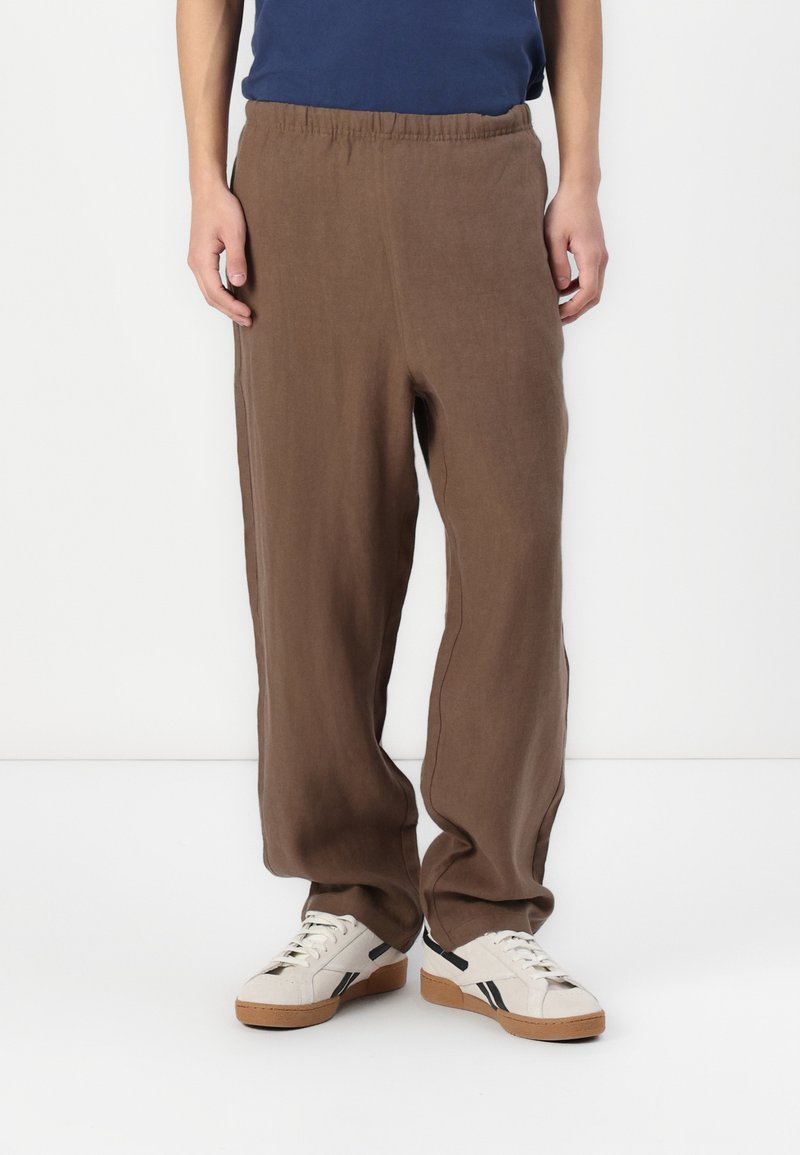 Pantalones de lino marrones con cintura elástica, con un corte relajado y patas rectas, combinados con zapatillas blancas.