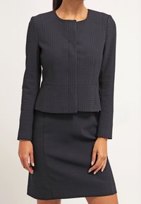 Abito blu scuro con blazer aderente caratterizzato da un sottile motivo a quadrati e maniche lunghe, abbinato a una gonna a matita coordinata.