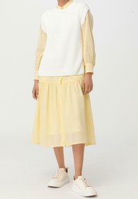 Biały prążkowany bezrękawnik nałożony na jasyellow sukienkę z guzikami, w połączeniu z beżowymi trampkami z grubą białą podeszwą.