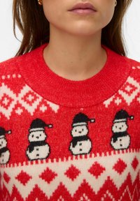 Roter Strickpullover mit einem Muster aus weißen Schneemännern mit schwarzen Hüten und einem Rautendesign in Cremefarbe am unteren Teil.