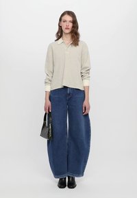 Pullover a righe chiare con colletto, abbinato a jeans in denim blu scuro a gamba larga. Accessoriato con una piccola borsa nera.