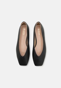 Zapatos planos negros con exterior de cuero suave, punta en forma de almendra y costuras mínimas. El forro interior es de un beige claro con una marca dorada.