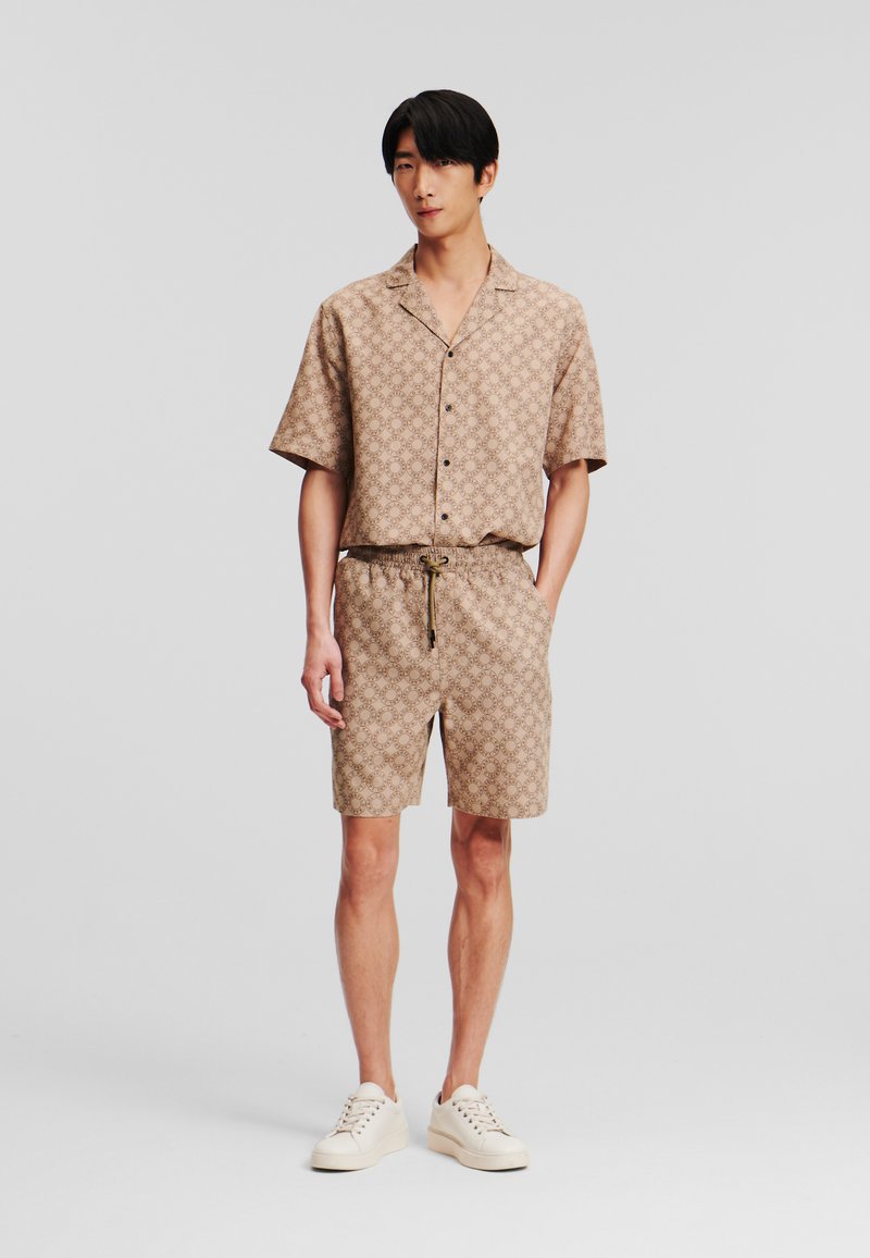 Conjunto de camisa de manga corta y pantalones cortos color beige con un patrón circular repetido. La tela es ligera y cuenta con una cintura con cordón.