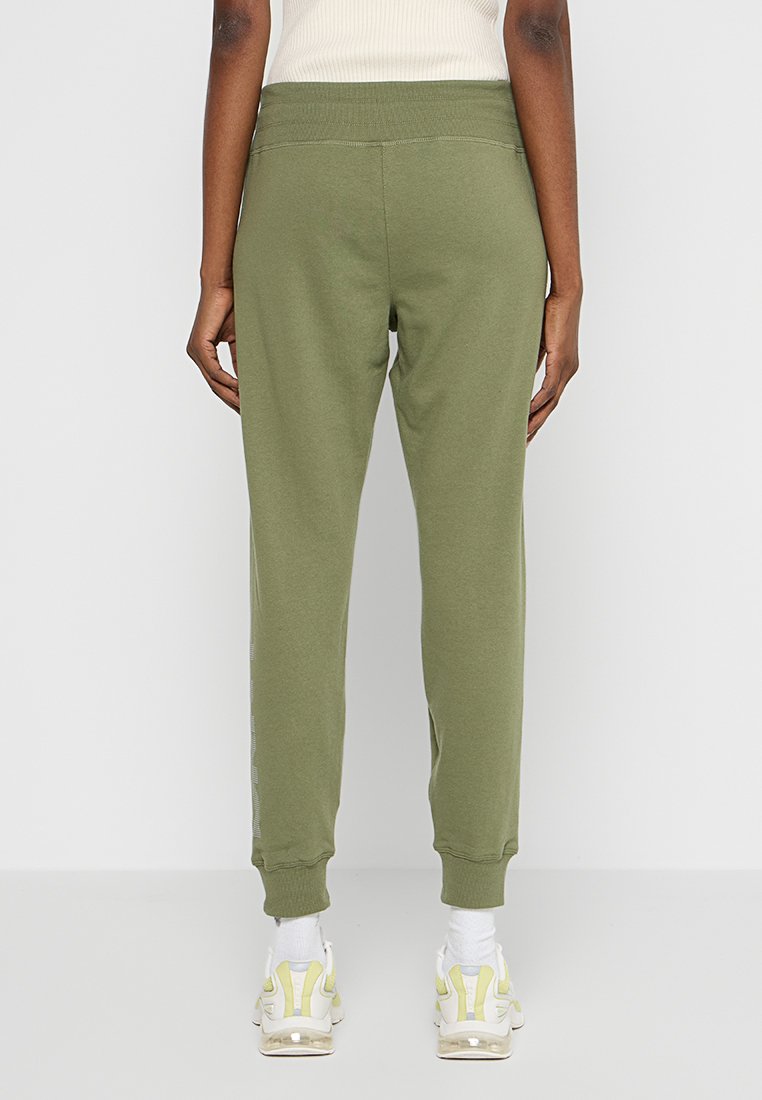 Joggers verdi in cotone con vita elastica, gambe affusolate e tasche. Abbinate a scarpe sportive bianche e gialle.