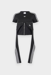 Μαύρο τοπ με κοντά μανίκια, λευκές ρίγες Adidas στα μανίκια, φερμουάρ μπροστά και επιπλέον υφασμάτινα πάνελ που κρέμονται με τρεις λευκές ρίγες.