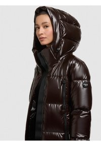 Pruun tuhmunud jope läikiva viimistlusega, suure üle pea tõmmatava kapuutsiga, tõmblukuga küljetaskute ja vasakul käel oleva ümmarguse logo plaastriga.