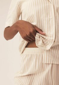 Beżowy zestaw dresowy w paski z miękkiego materiału, zawierający koszulę na guziki z krótkim rękawem oraz spodnie z elastycznym pasem, prezentujący luźny krój.