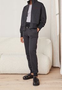 Black athletic set featuring a zippered cropped jacket with red stitching and matching tapered pants, complemented by black sandals.