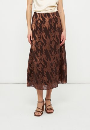 Ženska, ki nosi srednje dolgo krilo z abstraktnim vzorcem v rjavi in bakreni barvi, rjave sandale z visokimi petami in trakovi ter kremno brezrokavno majico.