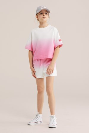 Meisje draagt een set met een wit en roze gradient T-shirt met korte mouwen en shorts, witte hoge sneakers en een lichtgrijze baseballpet.