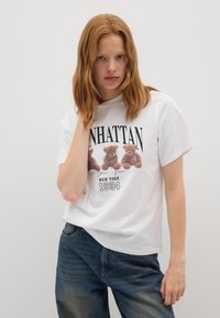 T-shirt in cotone bianco con grafica di tre orsetti e la scritta "MANHATTAN NEW YORK 1994." Vestibilità rilassata, maniche corte, scollo rotondo.