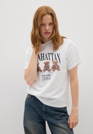 Camiseta blanca de algodón con un gráfico de tres ositos de peluche y el texto "MANHATTAN NUEVA YORK 1994." Ajuste relajado, mangas cortas, cuello redondo.
