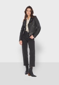 Black leather biker jacket with silver zippers, worn over a white blouse, paired with high-waisted black jeans and black heeled ankle boots.